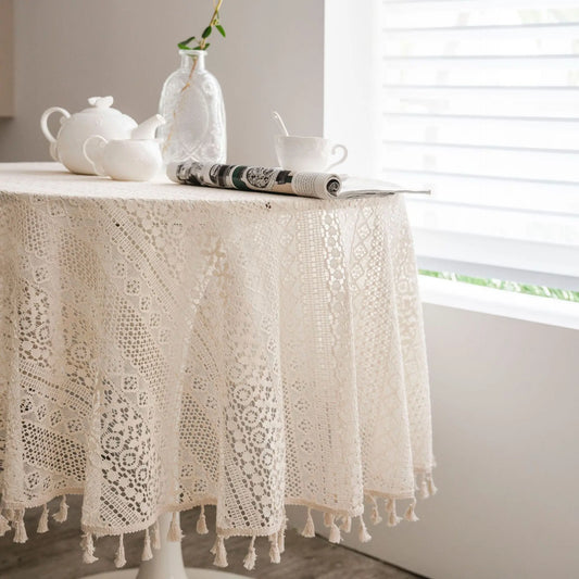 Lace tablecloth on a table with a teapot, cups, and a book in a bright room.