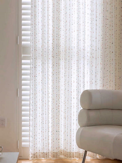 Sheer white curtain with a subtle pattern in a room with a light-colored sofa.