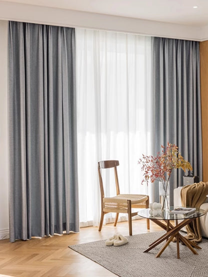 Living room with gray curtains, wooden chair, and glass coffee table.