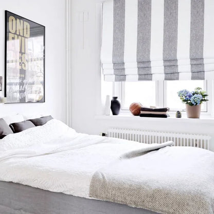 Neatly made bed in a bedroom with striped roman shade and decor.