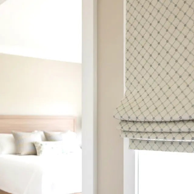 Patterned roman blind in a bedroom setting with a bed and neutral walls.