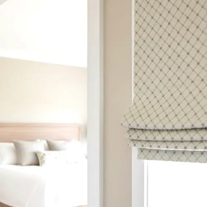 Patterned roman blind in a bedroom setting with a bed and neutral walls.