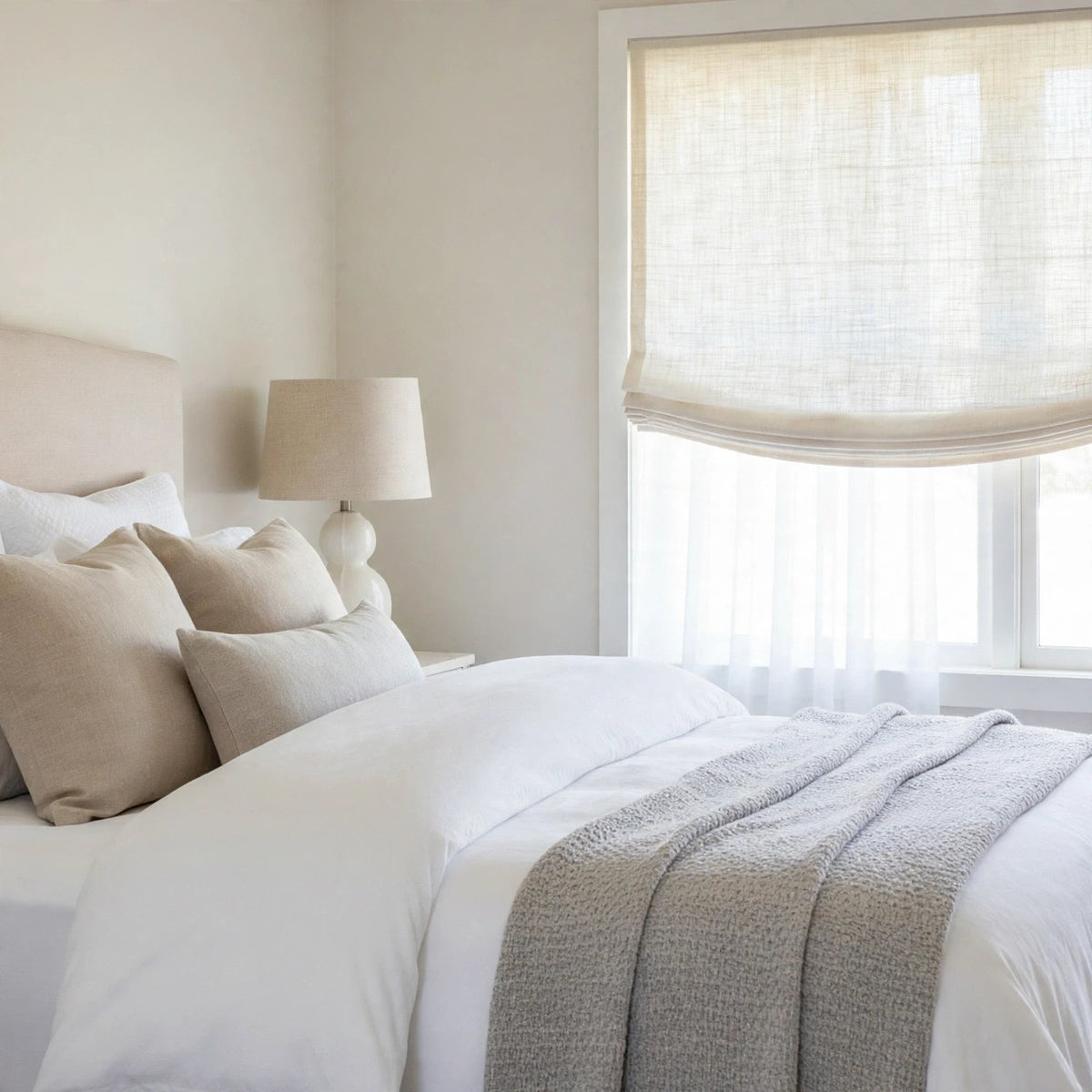 Ivory open weave sheer linen relaxed Roman shade with a soft curved bottom in a serene bedroom