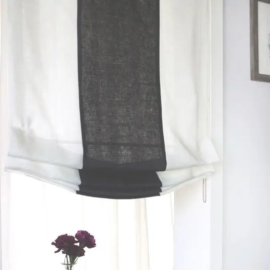 Black roman shade partially open on a window with a white curtain