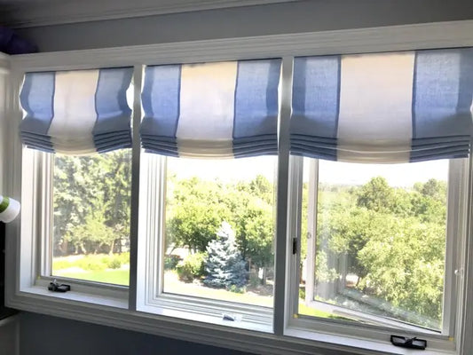 Window with blue and white striped linen roman shades and a view of trees outside.