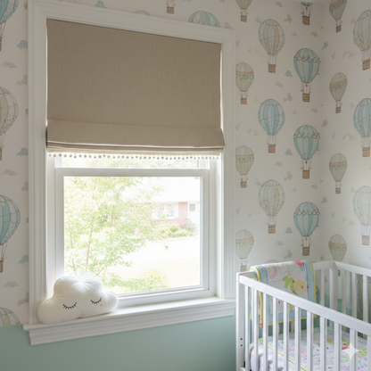 Nursery room with natural color blackout linen flat roman shade, crib, window, and hot air balloon-themed wallpaper.