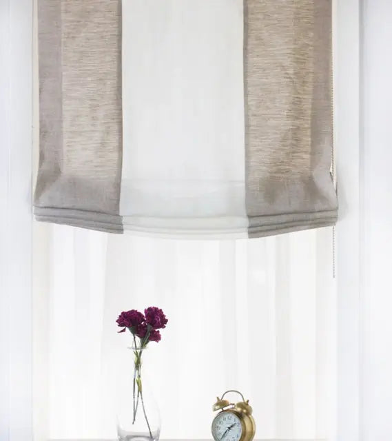 Window with natural and white color roman shades, a vase with purple flowers, and a clock on a white background
