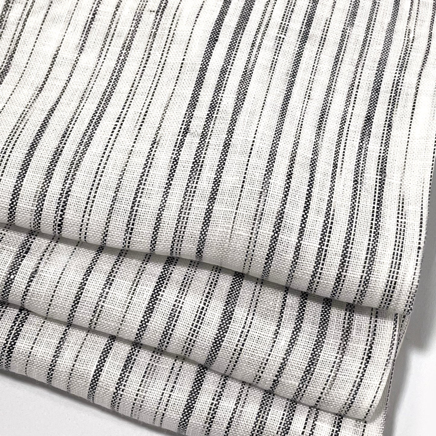 Close-up of a folded piece of linen fabric with a narrow irregular stripe pattern.