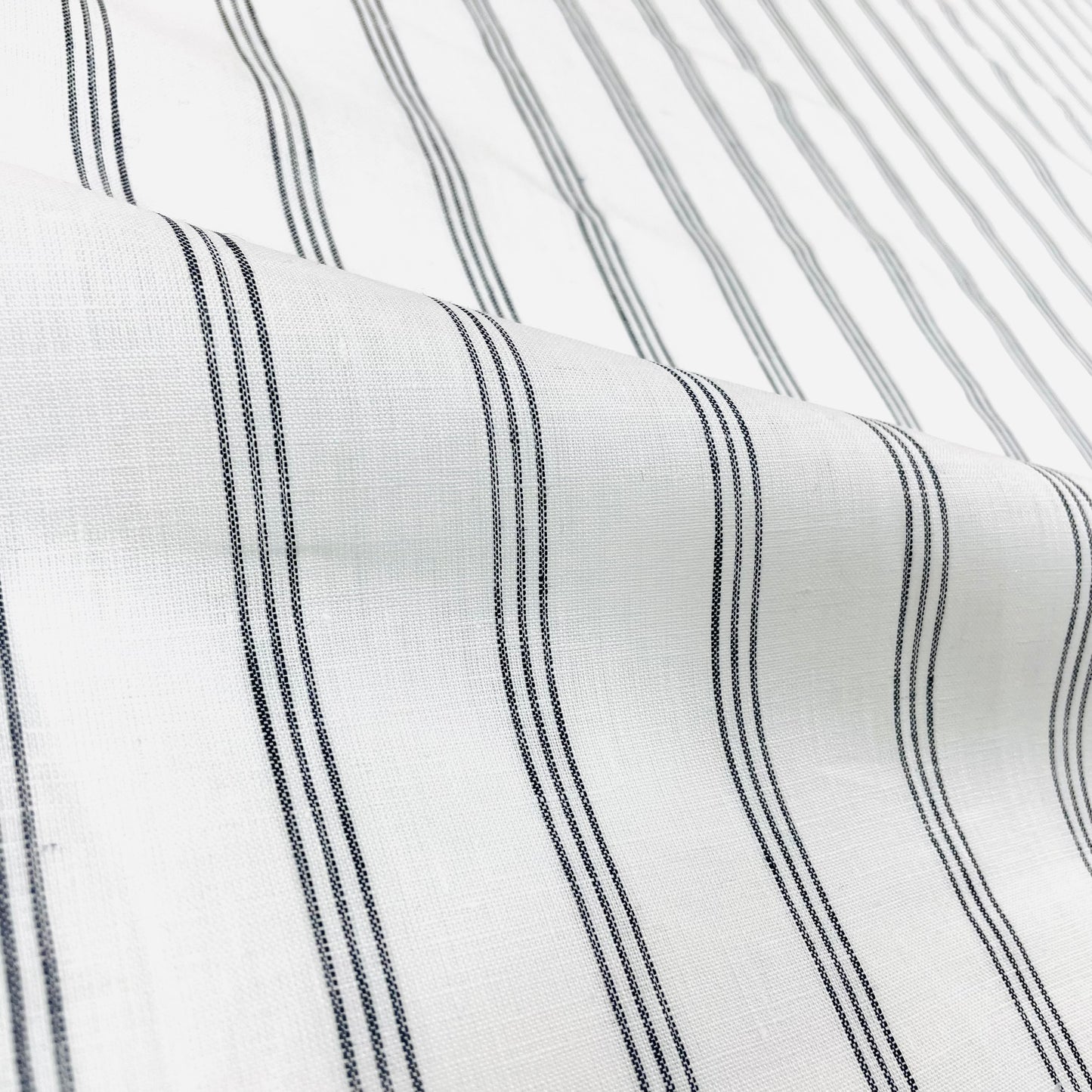 Natural white linen fabric with three thin dark grey vertical stripes.