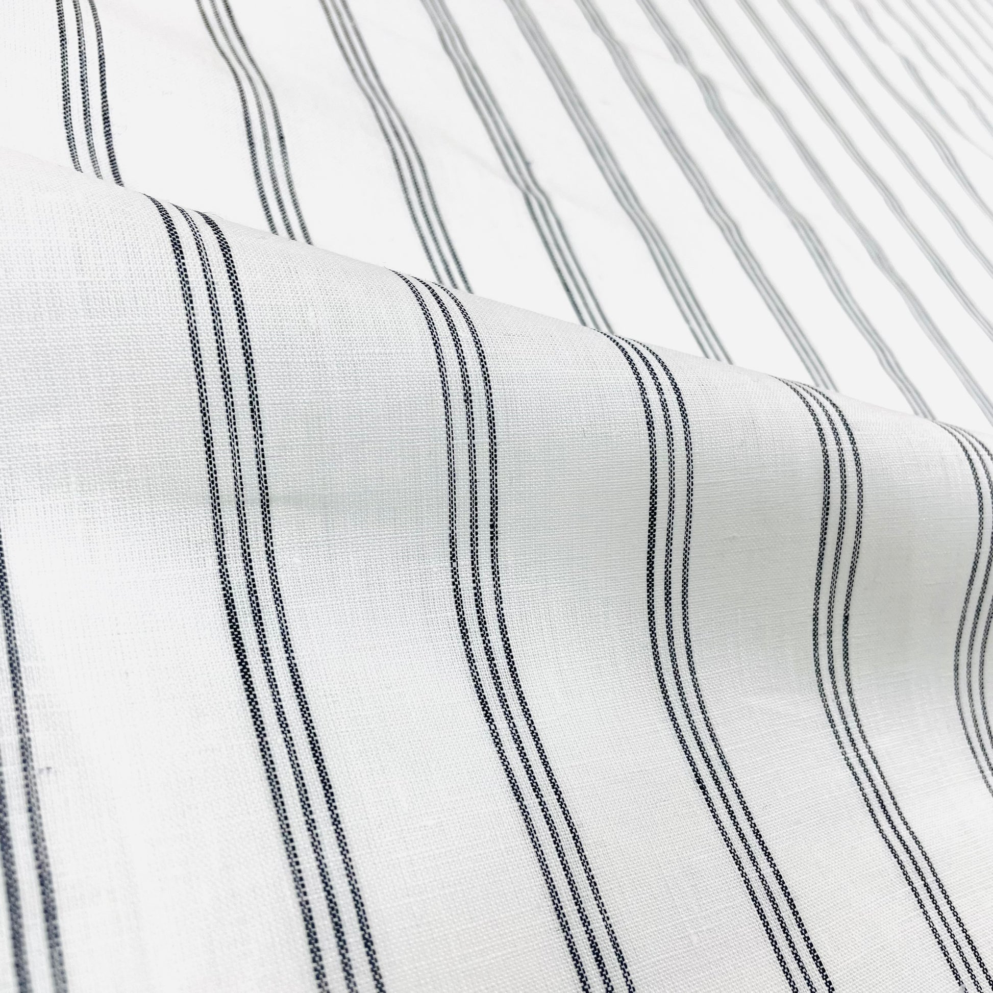 Natural white linen fabric with three thin dark grey vertical stripes.