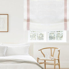 a white linen relaxed roman shade with pink, blush color decorative trim on the side in the bedroom.